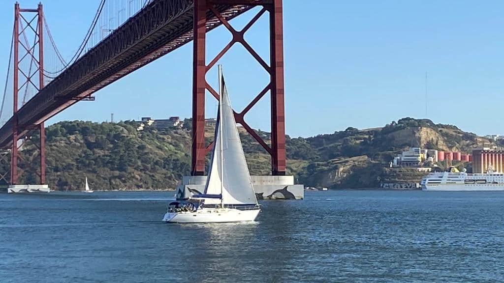 Sailboat sailing under the bridge over the Tagus River