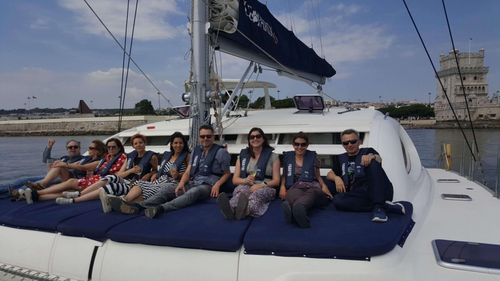 Personas sentadas en la proa del catamarán con la Torre de Belém al fondo