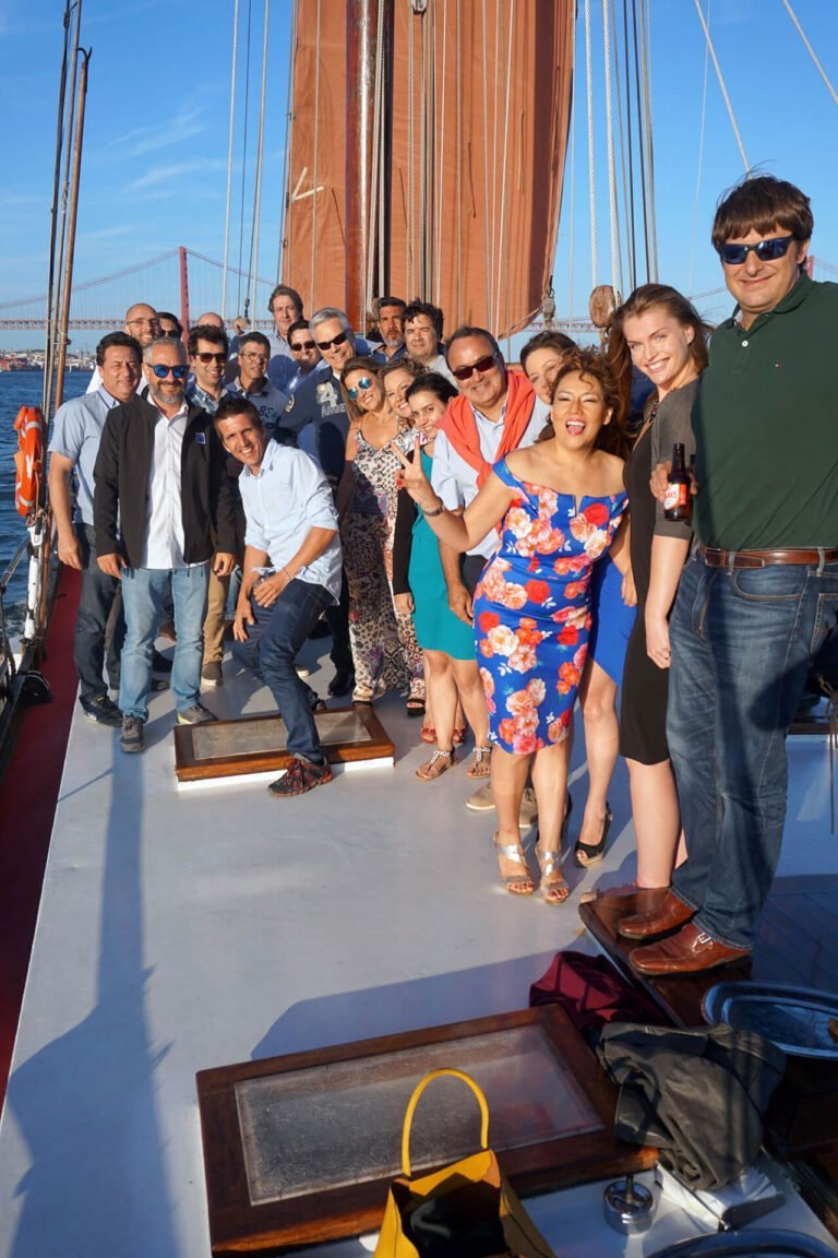 Group of people on a classic sailboat with the Tagus River Bridge in the background