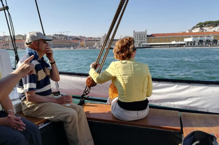 People aboard a classic sailboat viewing Commerce Square, the Sul e Sueste River Station and St. George's Castle in the distance
