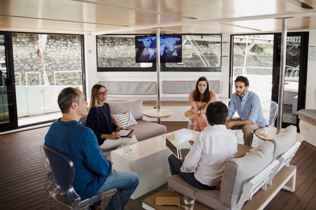 Un grupo reunido en la sala interior, en un ambiente de conversación y networking, con el río como telón de fondo. Una imagen ideal para transmitir la idea de reuniones informales, eventos corporativos o actividades de team building en un espacio acogedor y funcional.