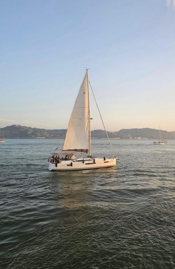 Veleiro branco Maharani a navegar com velas abertas no Rio Tejo ao pôr do sol