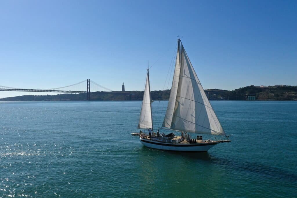 Sailboat sailing down Lisbon's Tagus River. In this image we can see the wonderful 25 de Abril Bridge as well as King Christ.