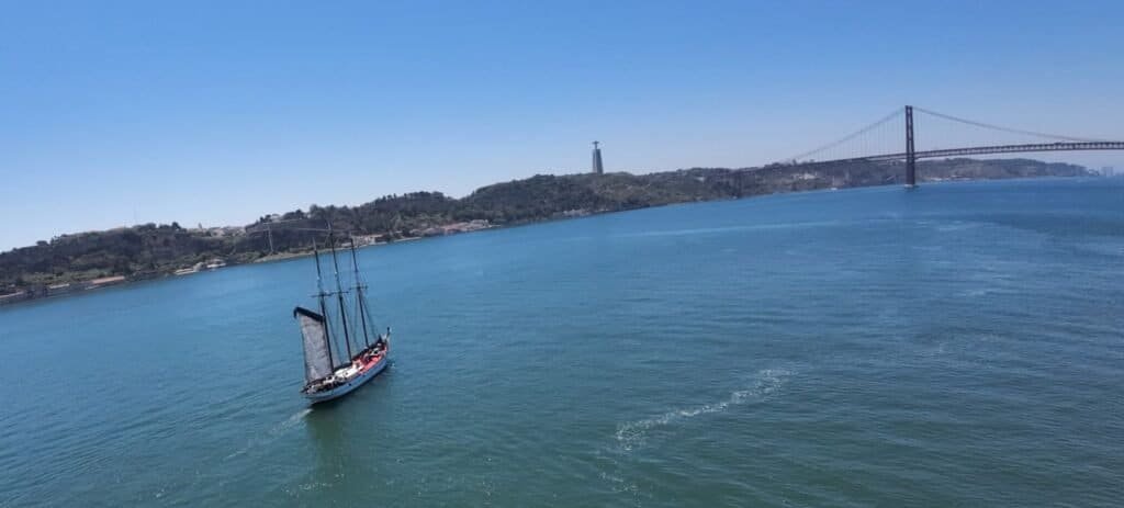 Sailboat sailing down the Tagus River, towards the 25th of April Bridge and King Christ