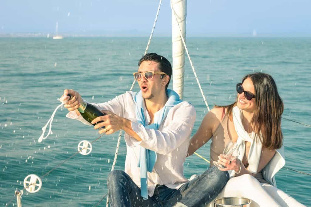 Young couple in love on a sailing boat toasting with a bottle of champagne - Happy girlfriend's birthday party on a luxury yacht cruise