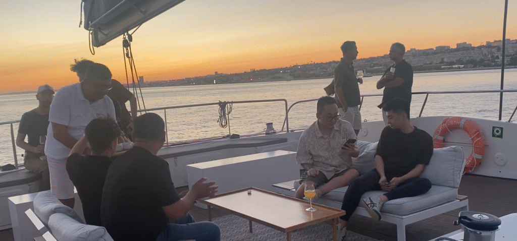 Convidados em convívio na zona superior do veleiro catamarã com a vista sobre Lisboa e sunset