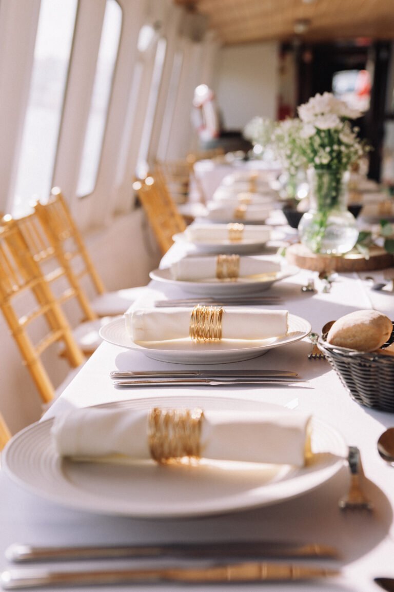 Elegant details stand out: porcelain plates, napkins with golden rings, and fresh flowers, evoking a luxury setting.