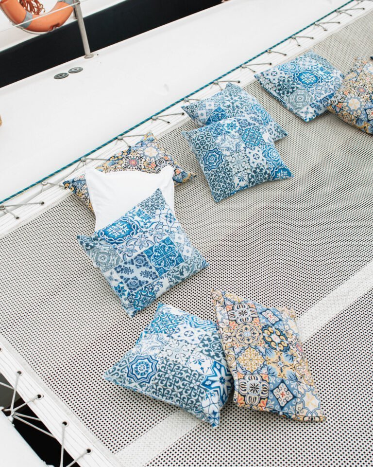 Várias almofadas com padrões de azulejos azuis e motivos náuticos estão espalhadas sobre a rede branca. Este é o local icónico do catamarã, onde os passageiros podem flutuar sobre o rio com total conforto.