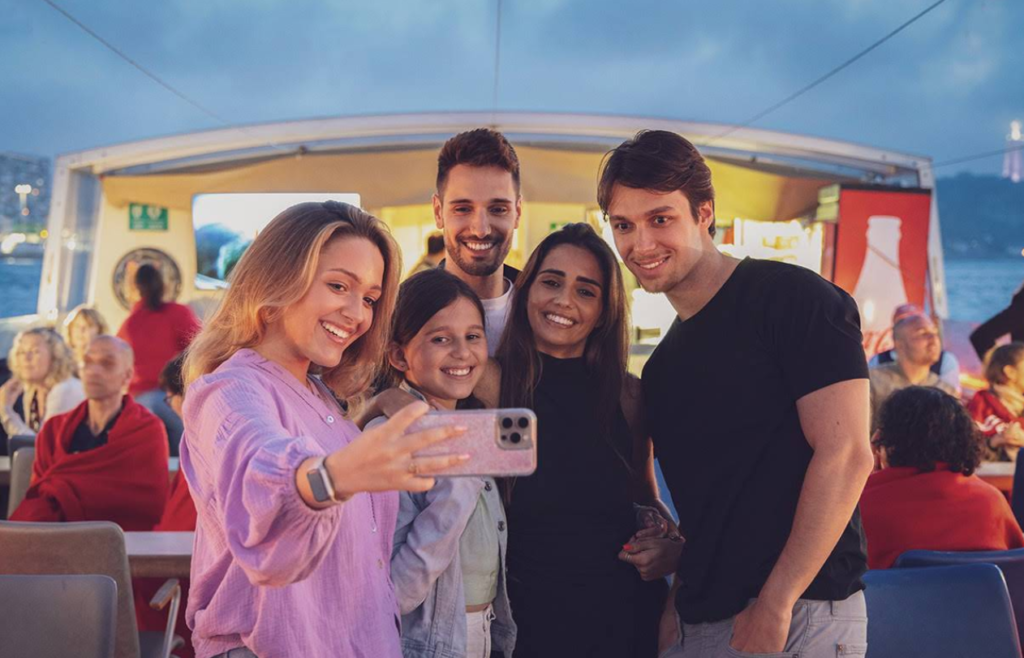 A group of friends celebrating and capturing memorable moments on the outdoor deck during an evening cruise.