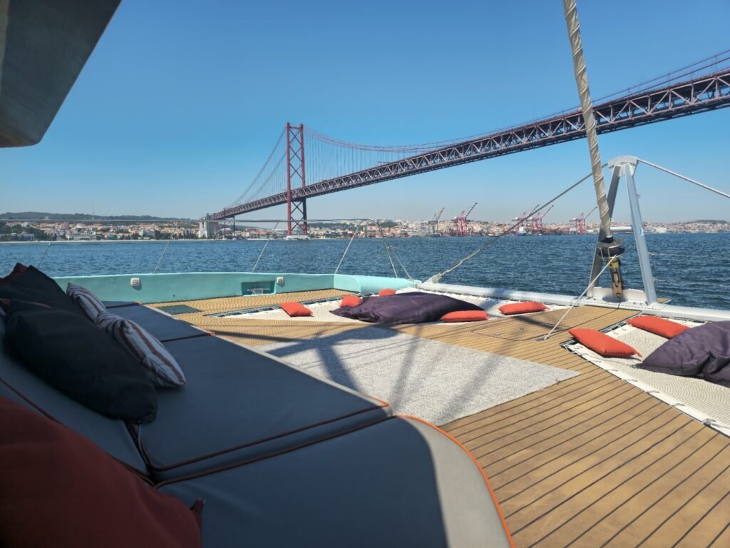 Amplia cubierta de madera de un catamarán con pufs para descansar y vistas al río Tajo
