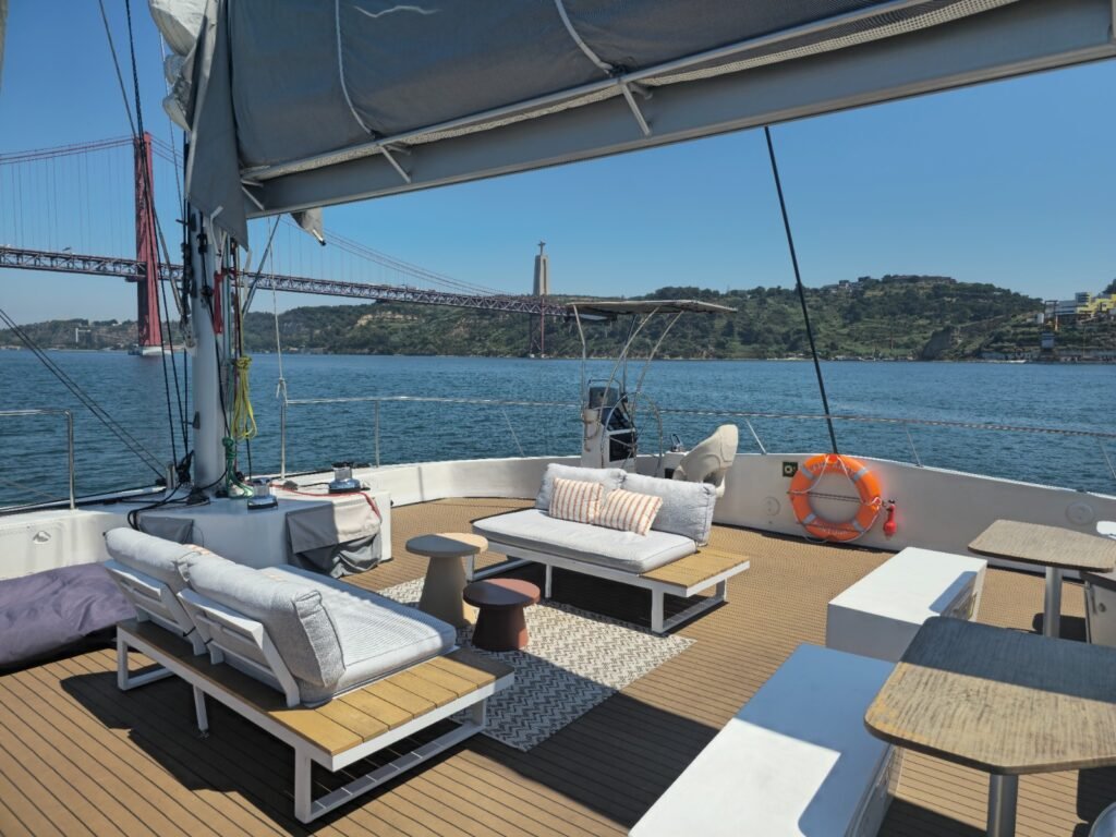 Mobiliario de exterior moderno en un catamarán, con sofás blancos y mesas, con el río Tajo como telón de fondo