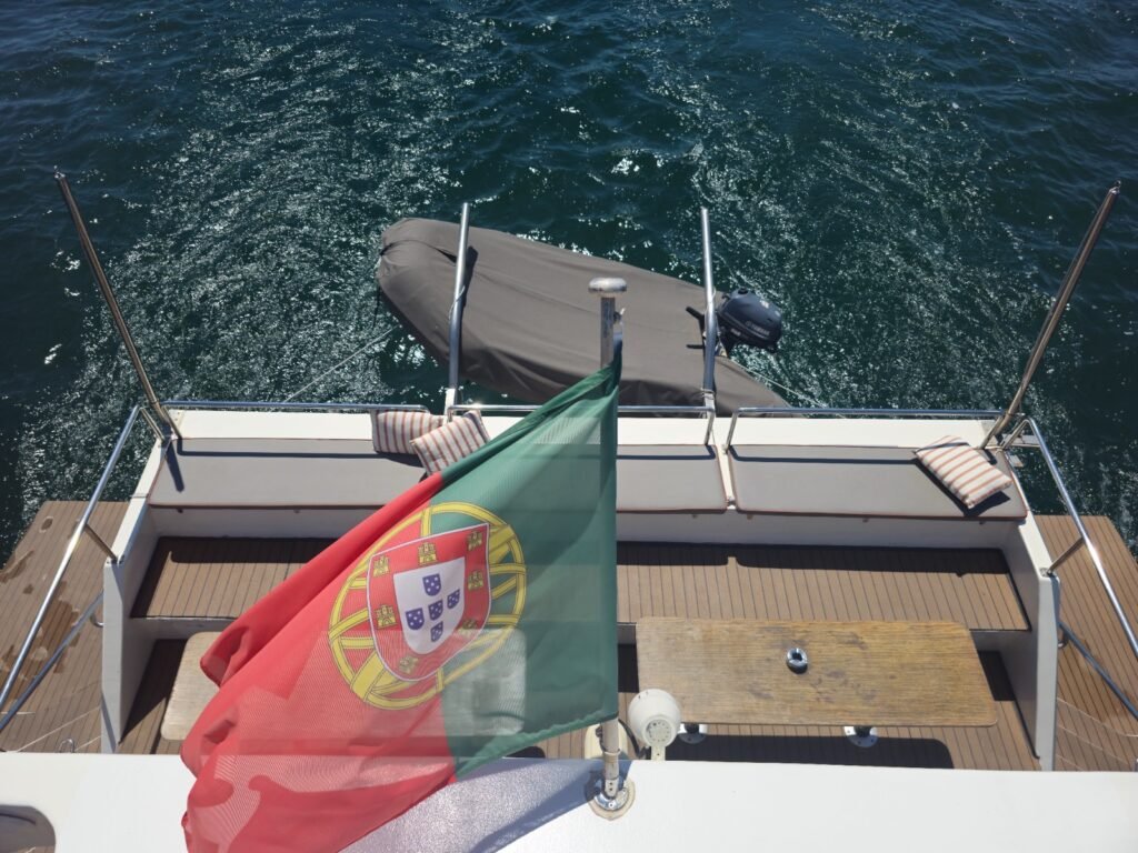 Popa del barco con la bandera de Portugal, vista desde arriba, mostrando la estela en el mar