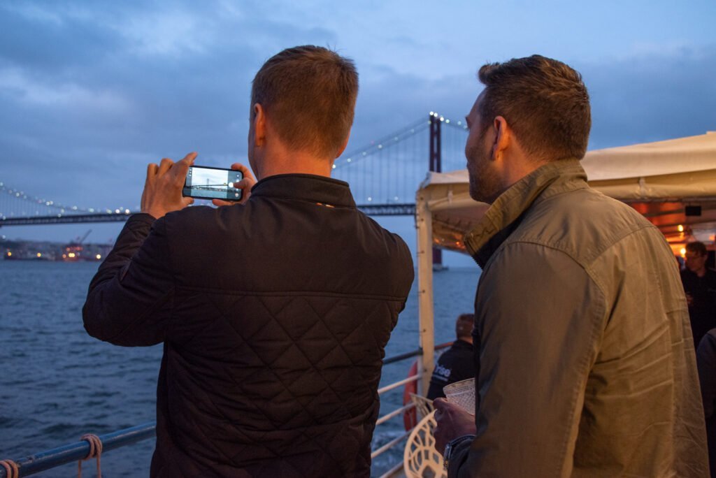 Convidados da ORISE capturam fotografias da Ponte 25 de Abril a partir do deck superior do barco Évora, deslumbrados com a beleza de Lisboa vista do rio.
