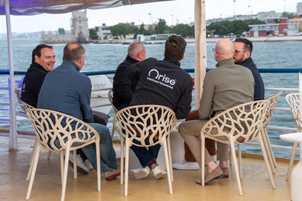 Los miembros del equipo de ORISE disfrutan del ambiente relajado en la cubierta superior del barco Évora, contemplando las vistas de Lisboa al atardecer