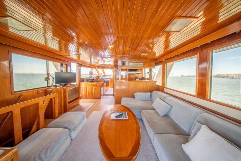 Salon principal du Trawler Alexander 56, avec ses canapés confortables aux teintes claires, sa table basse en bois, sa télévision et ses grandes baies vitrées offrant une vue sur Lisbonne.