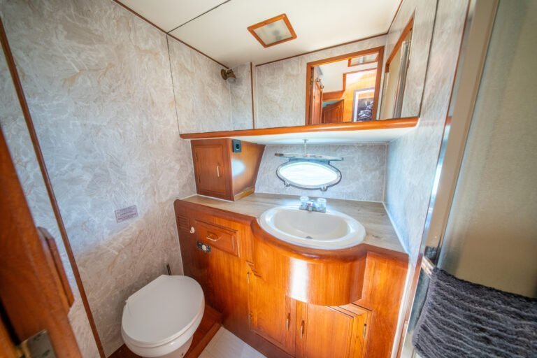 Salle de bains privative à bord du yacht Alexander 56, équipée d'un lavabo, de toilettes, d'un miroir et d'armoires en bois classique avec une finition nautique.