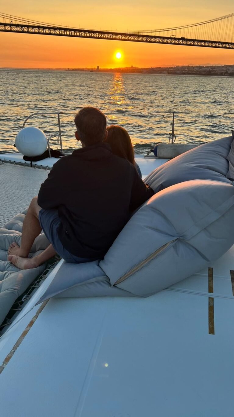 Momento de relaxamento ao pôr do sol a bordo do catamarã Corto Maltese III, na rede da proa, com vista sobre o rio Tejo. Passeio de sunset em catamarã em Lisboa, perfeito para casais e momentos românticos ao Sunset.